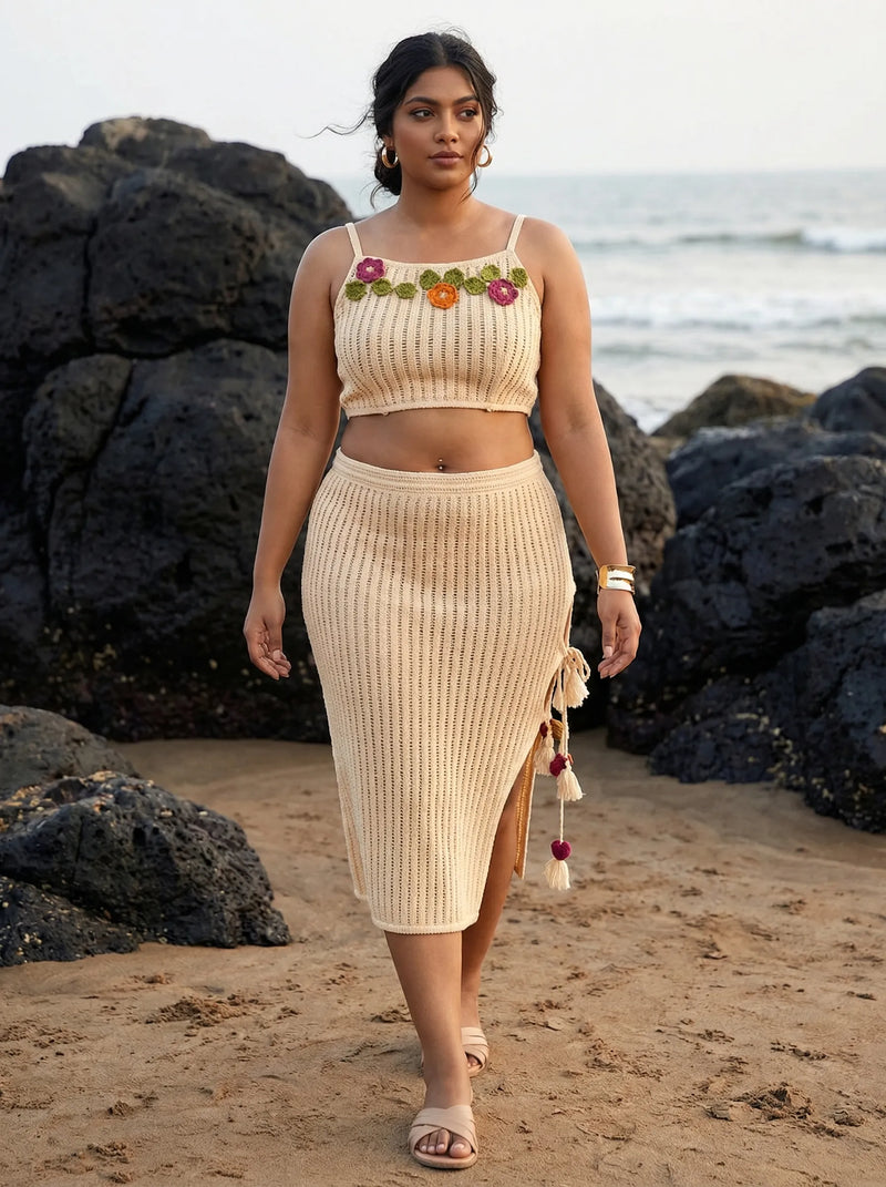 Woman in a beige outfit with floral details walking on a beach.