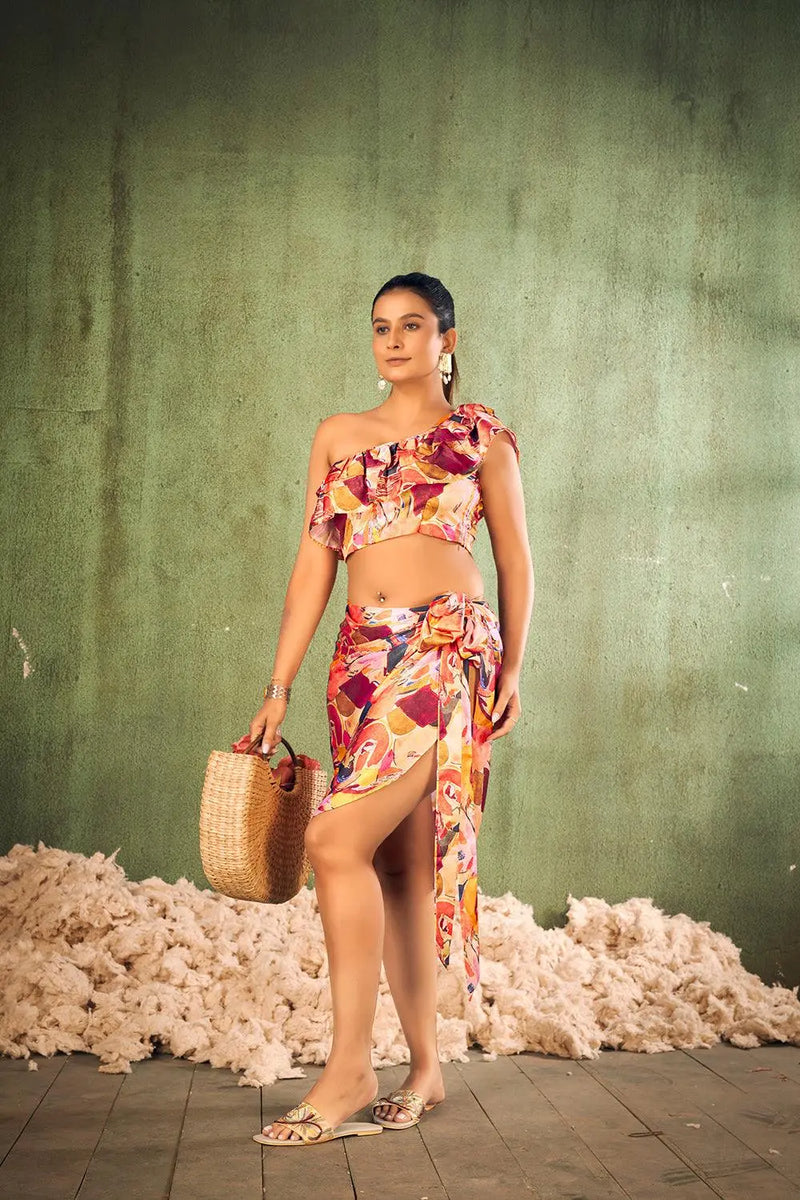 Woman in a colorful one-shoulder top and skirt standing against a textured green wall with white cotton on the ground. [Abstract Print Beach Wear - Plus Size - Women]