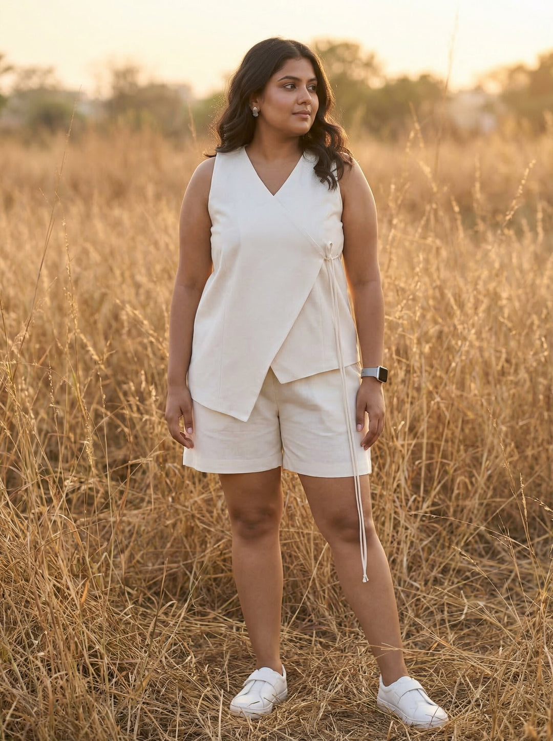 Woman in a white sleeveless top and shorts standing in a field with sunset lighting. [Buy Summer Co Ord Set for Women Online]