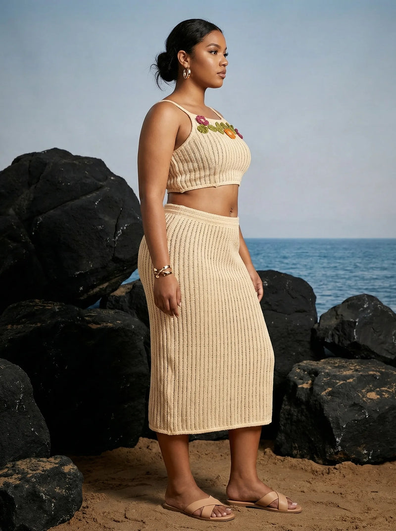 Woman in a beige outfit standing on a beach with rocks and ocean in the background